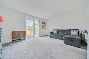 Spacious living room with grey carpet, large window, radiator, and corner sofa.