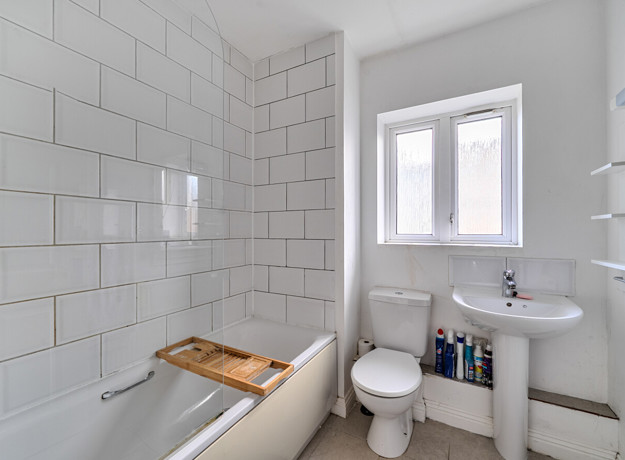 Bathroom with tiled walls, wash basin, toilet and window.