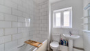 Bathroom with tiled walls, wash basin, toilet and window.
