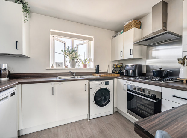 White kitchen with appliances, wood-effect worktops, and window above the sink.