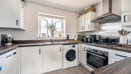 White kitchen with appliances, wood-effect worktops, and window above the sink.