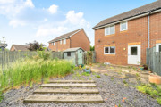 Back garden with paving, grass patches, shed, and neighboring houses in view.
