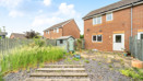 Back garden with paving, grass patches, shed, and neighboring houses in view.