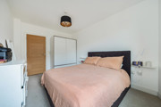 Carpeted bedroom with double bed, wardrobe, cehst of drawers and wooden door.