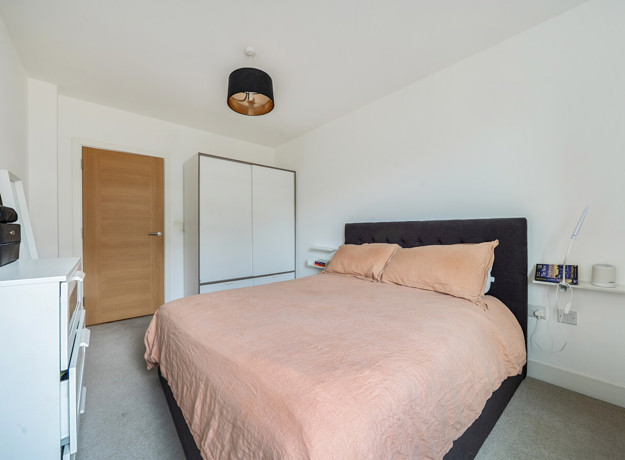 Carpeted bedroom with double bed, wardrobe, cehst of drawers and wooden door.