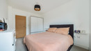 Carpeted bedroom with double bed, wardrobe, cehst of drawers and wooden door.