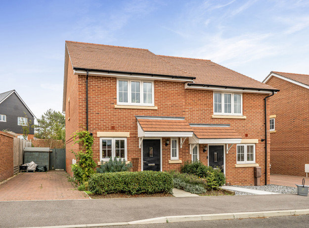 Semi-detached red brick house with driveway, small front garden and hedges.