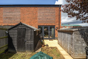 Rear garden with sheds, lawn and patio area and brick exterior of the house.