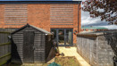 Rear garden with sheds, lawn and patio area and brick exterior of the house.