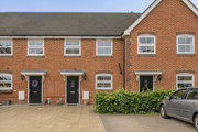 Exterior of a row of red brick terraced houses with parked cars and paved frontage.