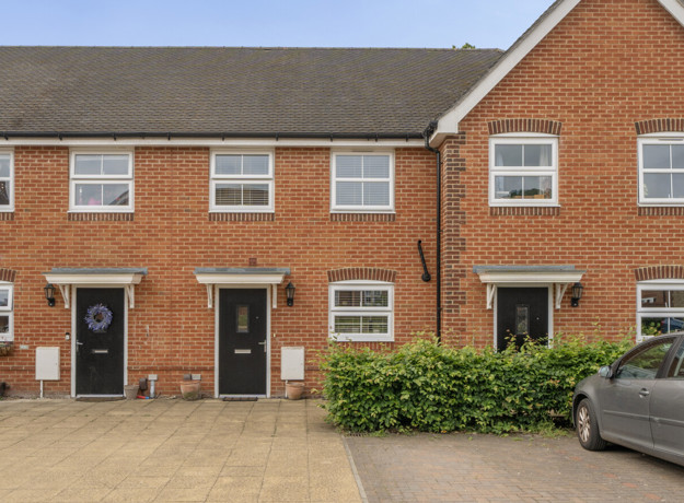 Exterior of a row of red brick terraced houses with parked cars and paved frontage.