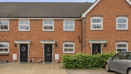 Exterior of a row of red brick terraced houses with parked cars and paved frontage.