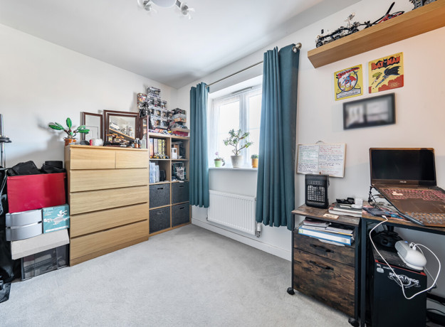 Bedroom with desk, drawers, shelving and window with curtains.