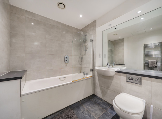 Bathroom with bath, shower screen, vanity unit, mirror and toilet.