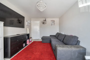 Living room with grey sofa, wall-mounted TV, and red carpet flooring.