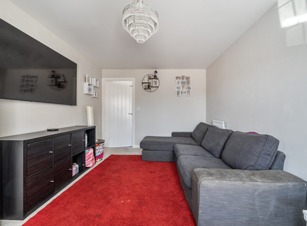 Living room with grey sofa, wall-mounted TV, and red carpet flooring.