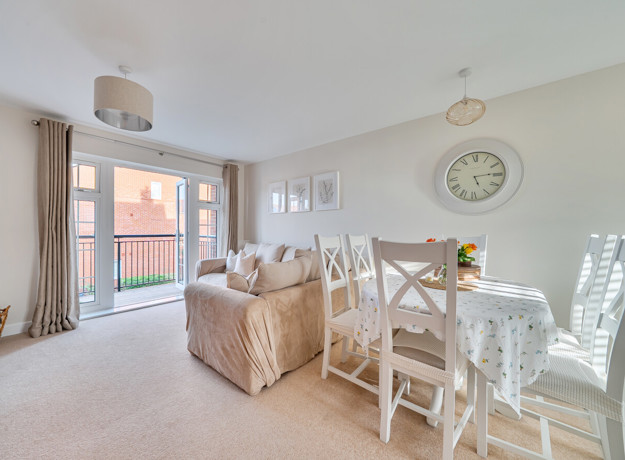 Open-plan living and dining area with table, chairs and balcony doors.