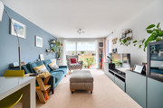 Living room with sofa, footstool, shelving unit and large window.
