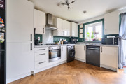 Kitchen with white cabinets, appliances, wooden-effect floor and door to garden.