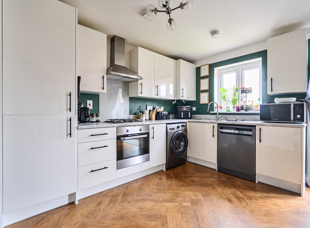 Kitchen with white cabinets, appliances, wooden-effect floor and door to garden.