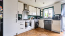 Kitchen with white cabinets, appliances, wooden-effect floor and door to garden.
