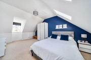 Bedroom with sloped ceiling, blue accent wall, neatly made double bed and white wardrobe.