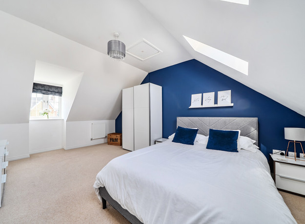 Bedroom with sloped ceiling, blue accent wall, neatly made double bed and white wardrobe.