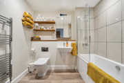 Bathroom with a bathtub, shower enclosure, toilet and wall-mounted shelves.