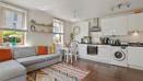 Open plan room with sofa, kitchen units, table, and window with blinds.