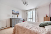 Bedroom with double bed, chest of drawers and window with curtains.