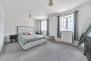 Bedroom with double bed, bedside table and two windows with curtains.