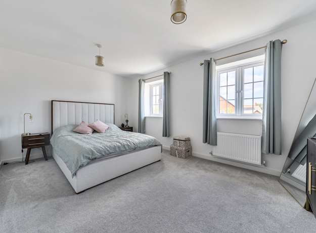 Bedroom with double bed, bedside table and two windows with curtains.