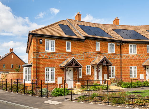 Row of red-brick terraced houses with front gardens and solar panels on roofs. (1)