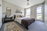 Bedroom with bed, bedside table, mirror, rug, and large windows with curtains.