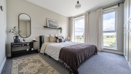 Bedroom with bed, bedside table, mirror, rug, and large windows with curtains.