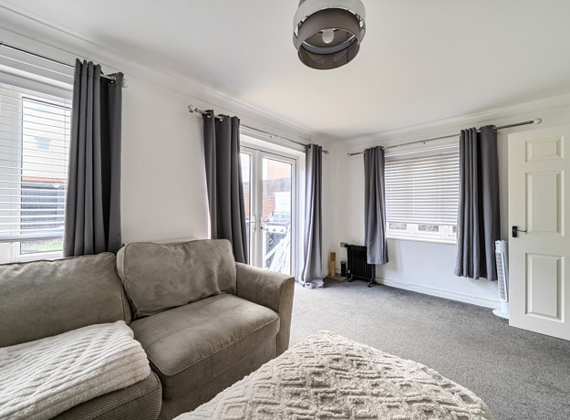 Living room with sofa, multiple windows, patio doors and carpeted flooring.