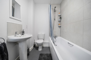 Bathroom with bathtub, shower, sink, and toilet in neutral tones.