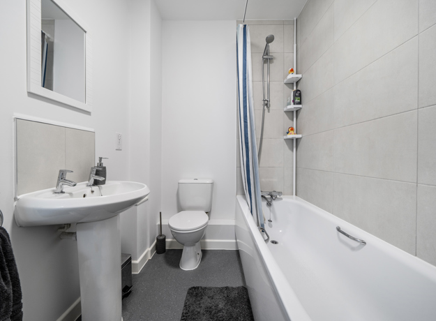 Bathroom with bathtub, shower, sink, and toilet in neutral tones.
