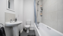 Bathroom with bathtub, shower, sink, and toilet in neutral tones.