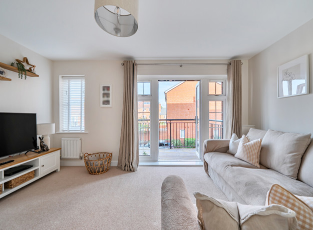 Living room with sofas, TV unit and doors leading to a balcony.