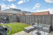 Garden with patio seating, lawn, and wooden fencing under blue sky.
