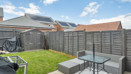 Garden with patio seating, lawn, and wooden fencing under blue sky.
