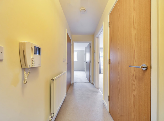Hallway with intercom, wooden doors and carpeted floor.