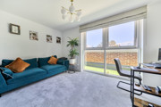 Living room with sofa, desk, large window, plant and wall art.