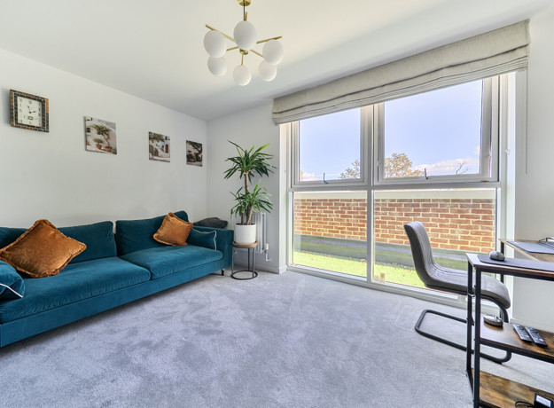 Living room with sofa, desk, large window, plant and wall art.