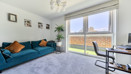 Living room with sofa, desk, large window, plant and wall art.