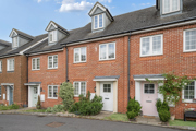 Red brick mid-terrace house with white doors and dark slated roof.