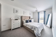 Bedroom with double bed, chest of drawers and windows with curtains.