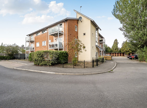 Apartment building with parking spaces, trees and surrounding pathways.