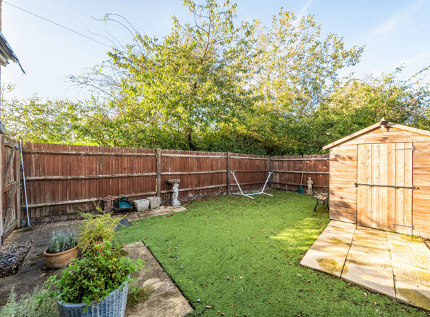 Garden with lawn, paved patio, wooden shed and surrounding fencing. (1)